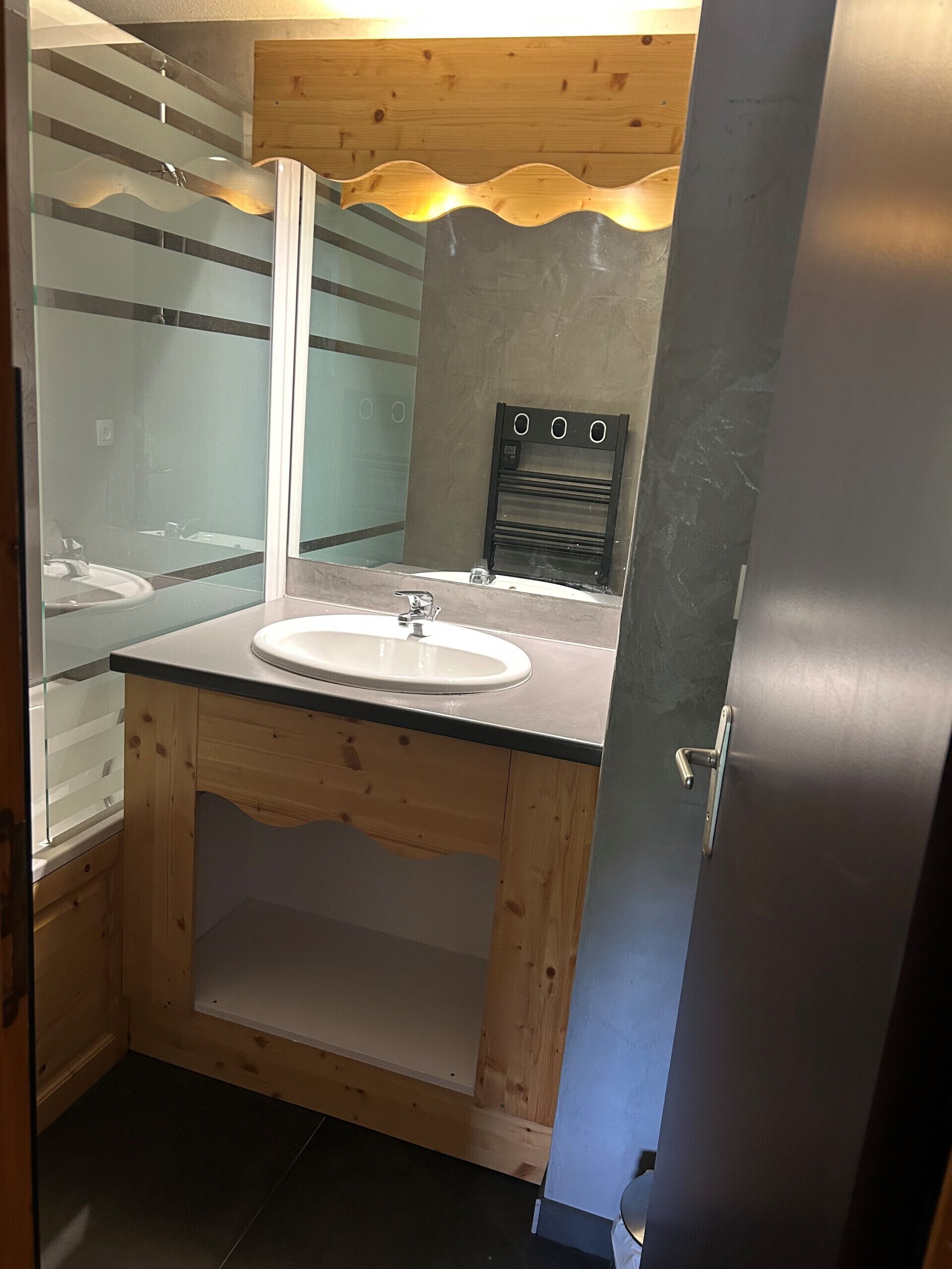 Ein Badezimmer mit einem Holzkosmetikschrank, einem weißen Waschbecken und einem Spiegel.