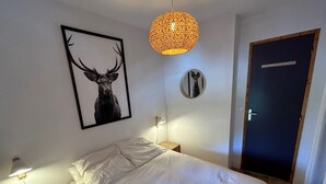 A neatly made bed with white linens, a framed deer picture on the wall, a round mirror, and a door with a wooden frame. - Apt 4 ppl, balcony, near the ski runs (Modane)