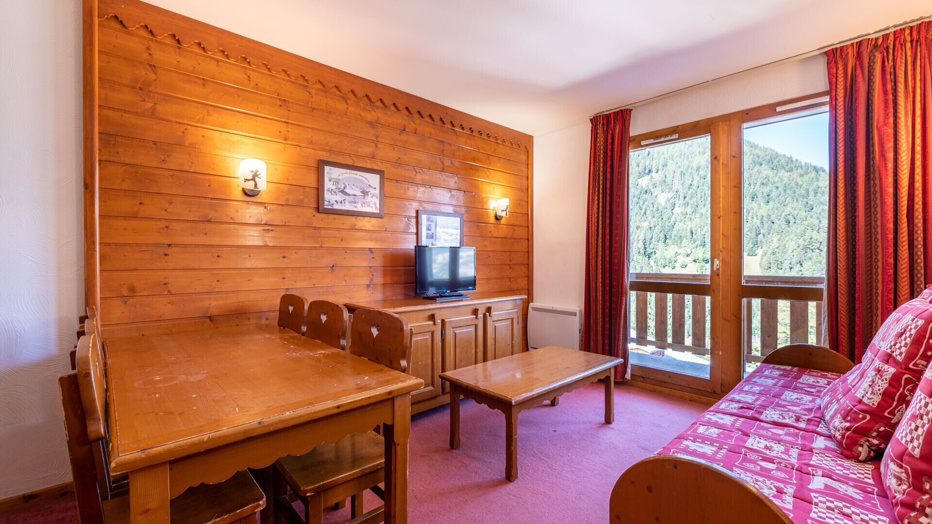 A cozy room with a wooden wall, a TV, a dining table, and a sofa.