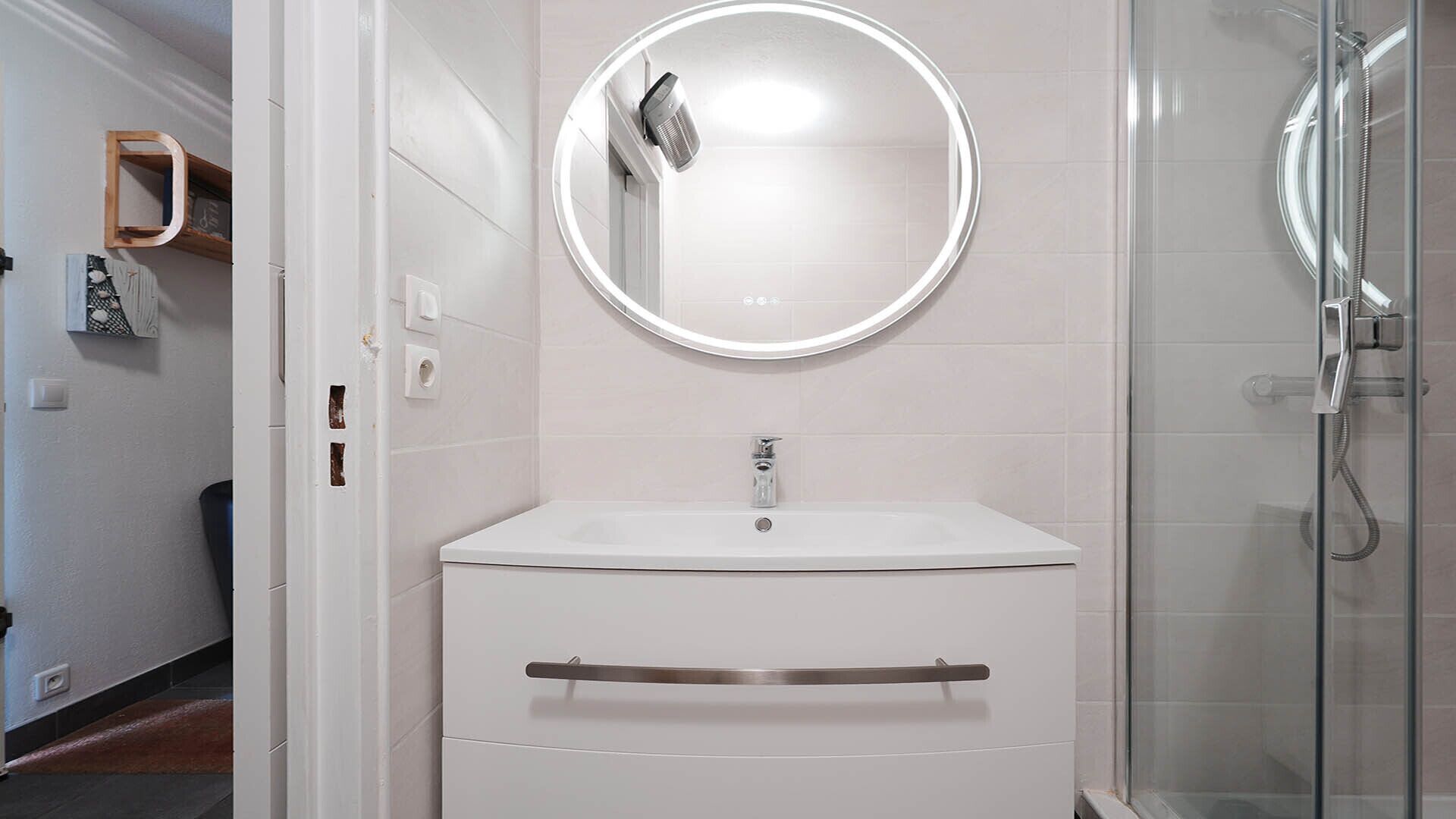 A bathroom with a white sink, a round mirror, and a glass shower enclosure.