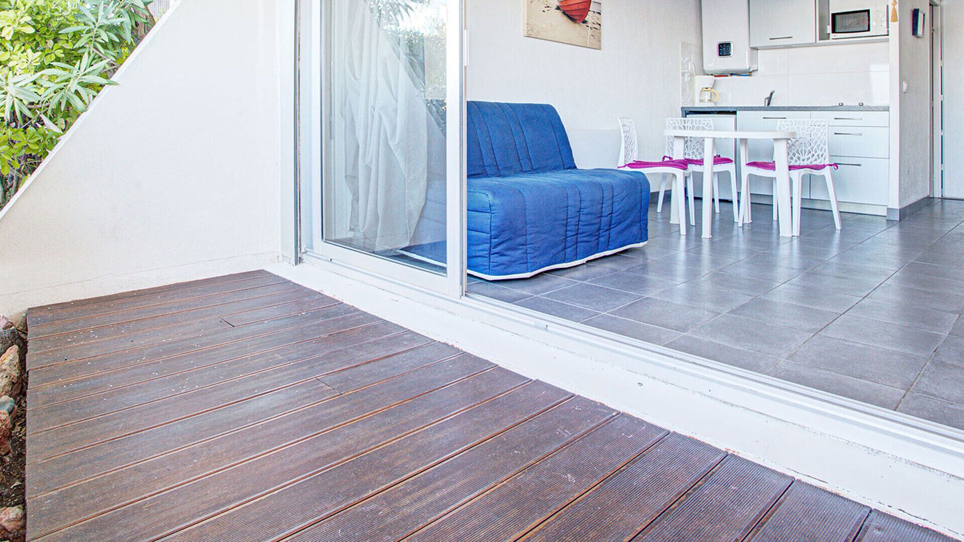 A modern room with a wooden deck, a blue sofa, and a kitchen area with white appliances.