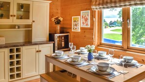 Un intérieur en bois avec une table à manger pour quatre personnes, des meubles blancs et une fenêtre donnant sur un paysage verdoyant.