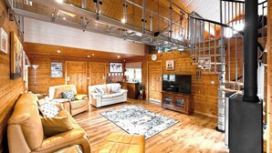 Un salon spacieux avec un plafond haut, des murs en bois, une grande télévision et une cheminée.