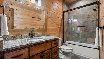 A bathroom with a wooden vanity, a granite countertop, a white toilet, and a glass-enclosed shower area.