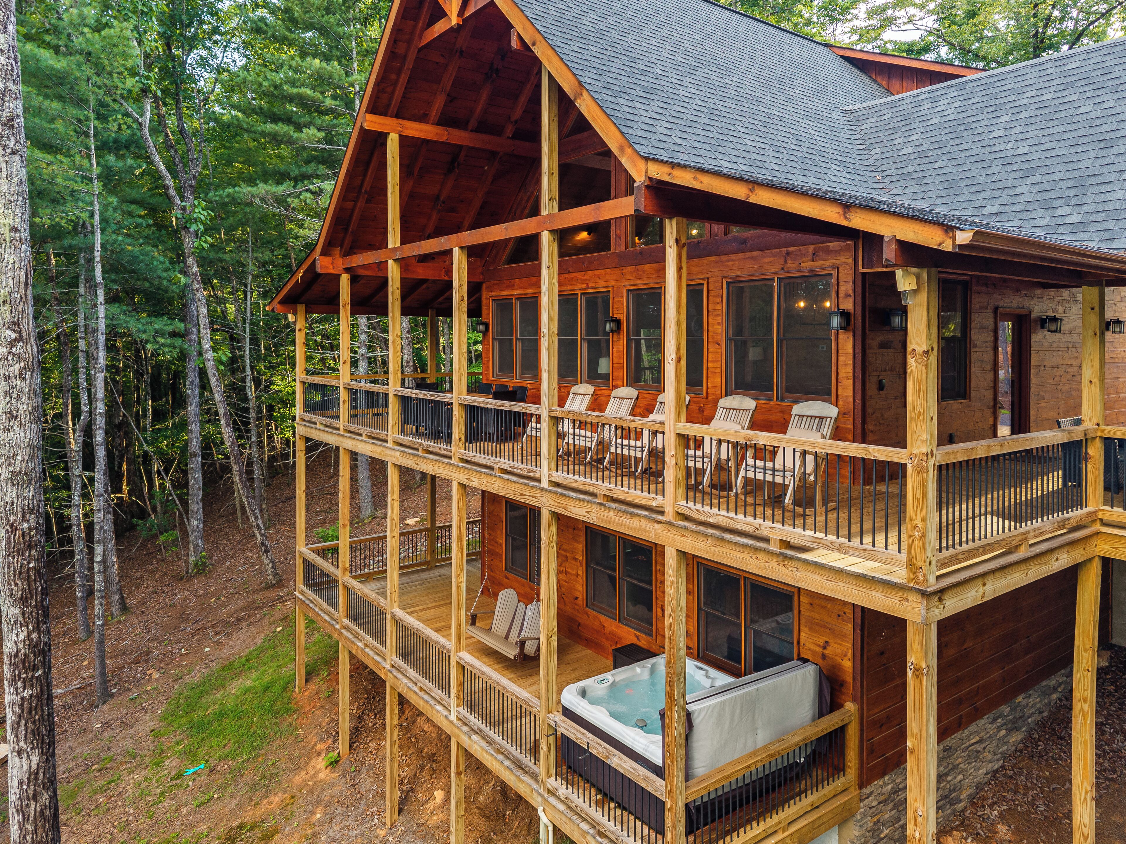 A two-story log cabin with a balcony, outdoor seating, and a hot tub.