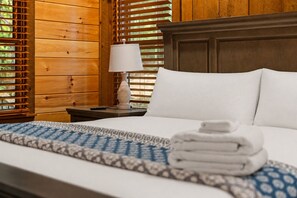 A neatly made bed with white linens, a folded towel, and a bedside lamp on a wooden nightstand.