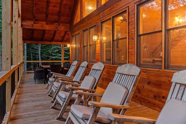 A wooden deck with several Adirondack chairs and a table, overlooking a forested area.