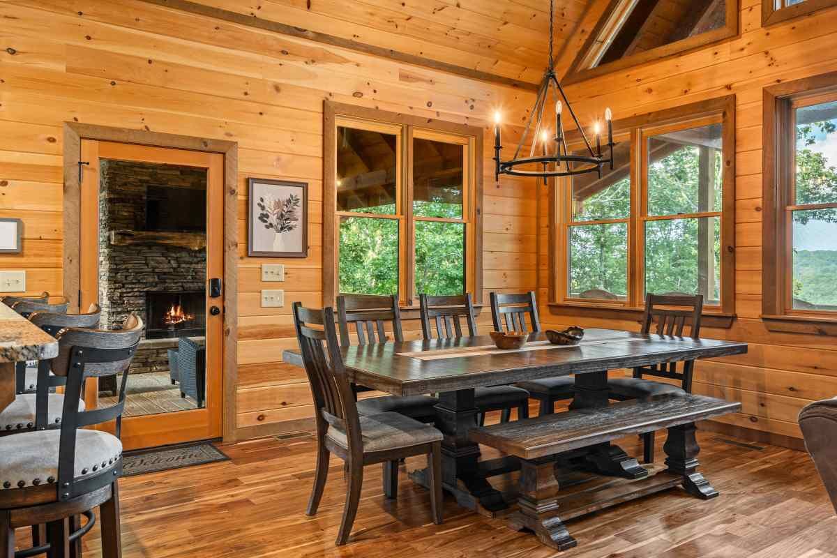 A wooden interior with a fireplace, a dining table, and large windows.