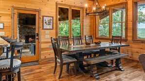 Un interior de madera con chimenea, una mesa de comedor y ventanas grandes.