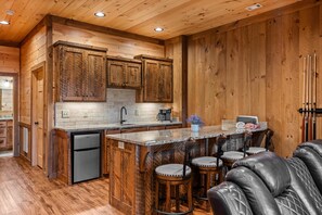 A kitchen with wooden cabinets, a refrigerator, a sink, and a bar area with stools.