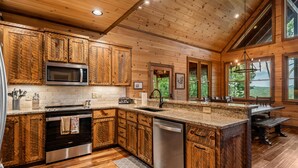 A spacious kitchen with wooden cabinets, a microwave, a stove, and a dishwasher. - Spacious mountain cabin w/mountain views, hot tub & game room! (Cherry Log)