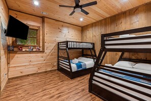 Camera da letto in una baita di legno con letti a castello, una ventola a soffitto, una TV a parete e una finestra con persiane.
