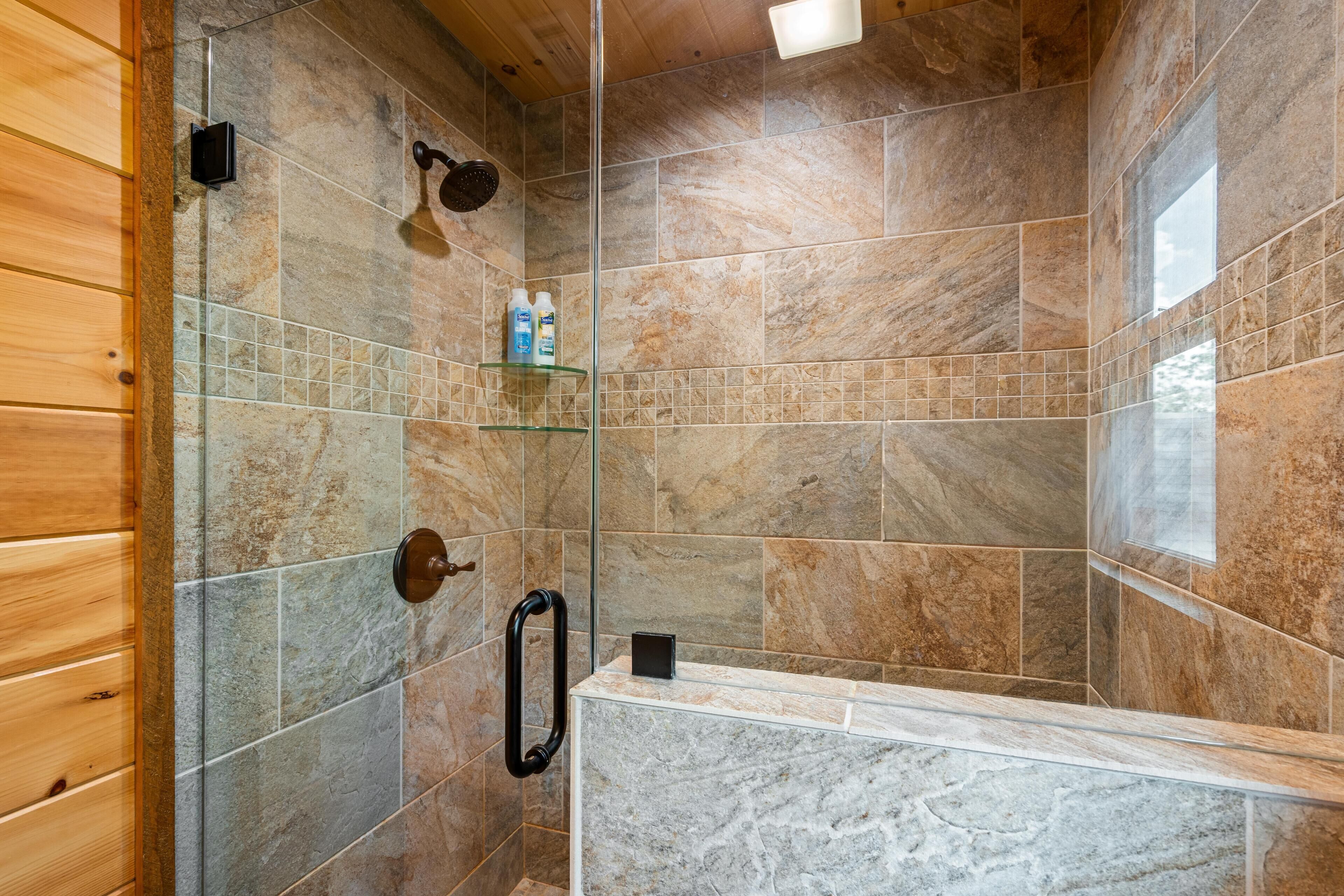 Un espace douche avec des carreaux de pierre, une étagère en verre pour les articles de toilette et une porte en bois.