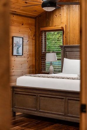 A wooden-paneled room with a bed, a lamp, and a window with blinds. - Spacious mountain cabin w/mountain views, hot tub & game room! (Cherry Log)