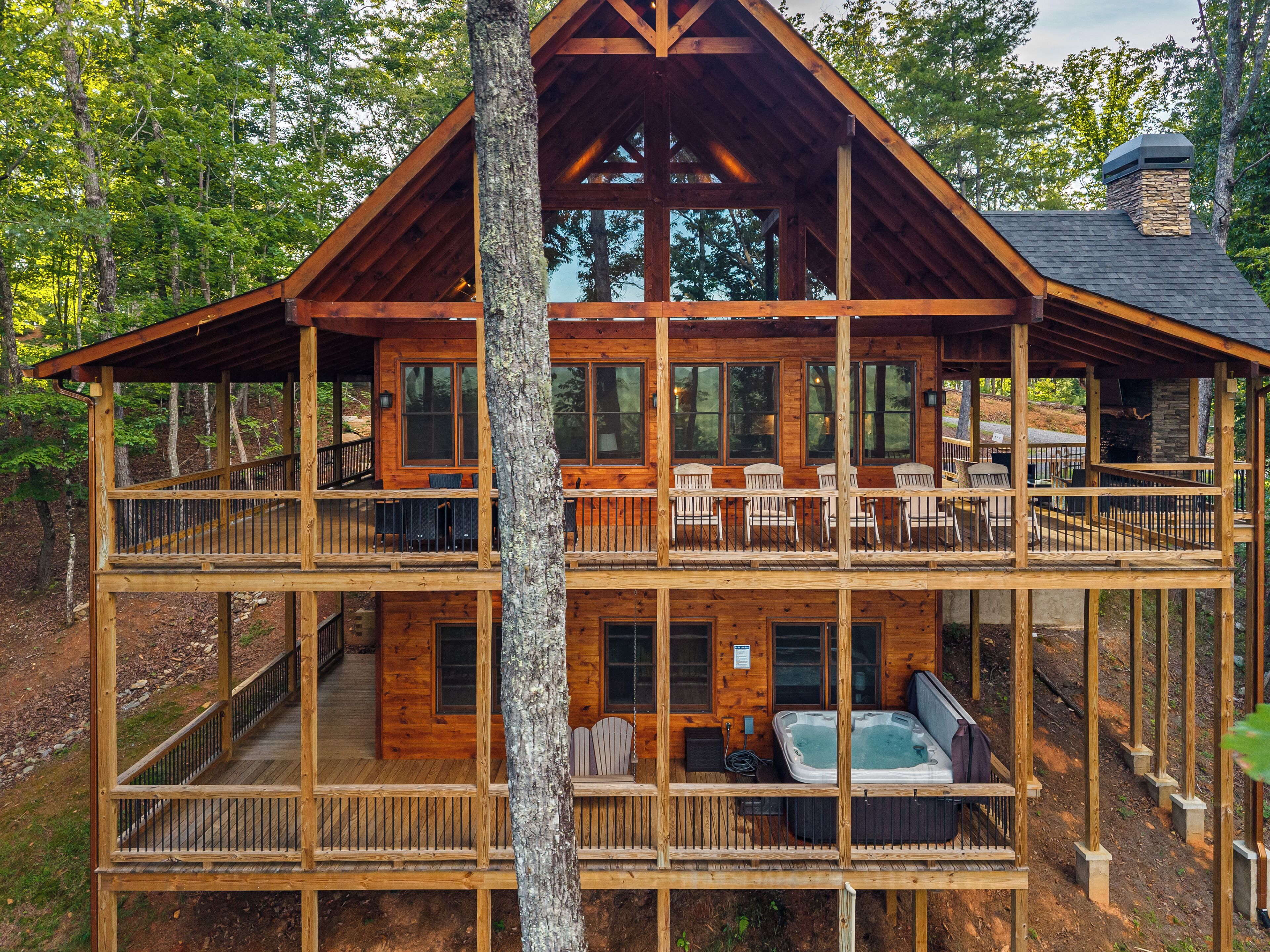 Een houten chalet met twee verdiepingen, een balkon, buitenmeubels en een jacuzzi.