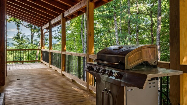 A covered outdoor area with a grill, wooden deck, and a view of a forest. - Spacious mountain cabin w/mountain views, hot tub & game room! (Cherry Log)