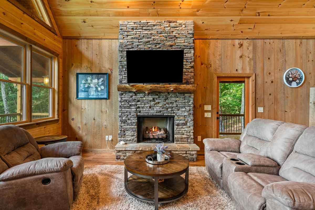 A cozy living room with a stone fireplace, leather sofas, and a flat-screen TV.