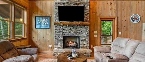 Una sala de estar acogedora con chimenea de piedra, sofás de cuero y televisor de pantalla plana.