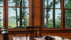 A wooden interior with a table and chairs, large windows with a view of trees and hills. - Spacious mountain cabin w/mountain views, hot tub & game room! (Cherry Log)
