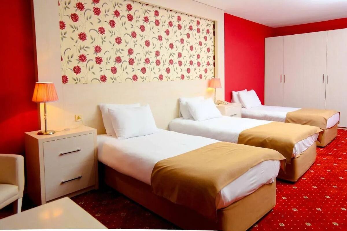A hotel room with two beds, a red carpet, a white wardrobe, and a floral wallpaper.