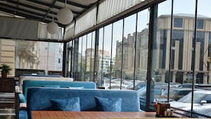 Un interior moderno con ventanas amplias, asientos en tonos azul y amarillo, y vistas a edificios de la ciudad.
