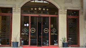Entrada de hotel con alfombra roja, puertas dobles y un cartel con el nombre del hotel.