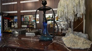 Una zona de bar con un narguilé, una encimera de mármol y estanterías llenas de botellas.