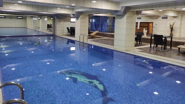 Una amplia piscina interior con agua cristalina, rodeada por una pared de azulejos y una zona de estar con sillas y mesas.