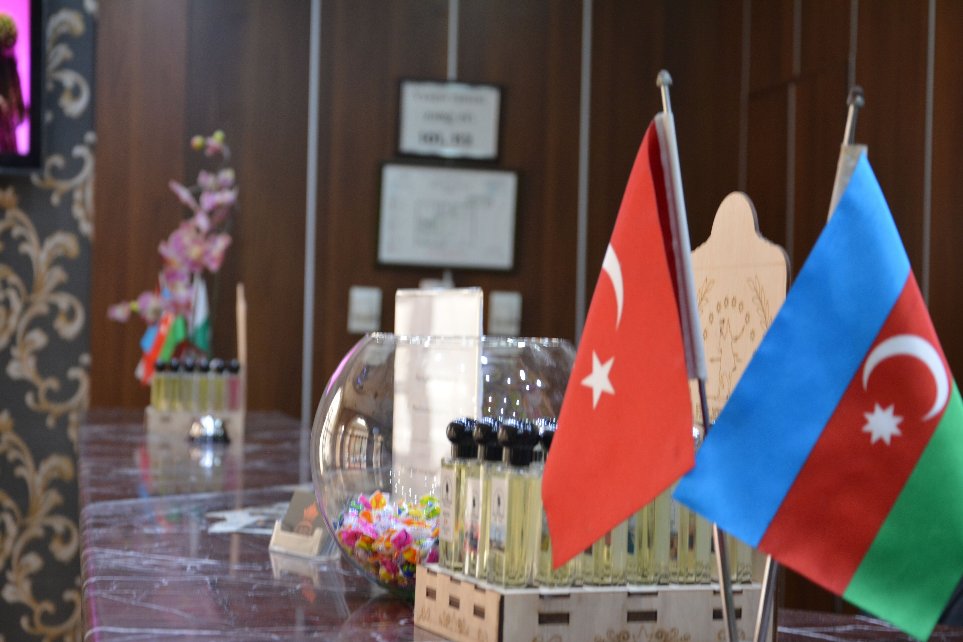 A table with flags, a glass container with colorful items, and a decorative piece in the background.