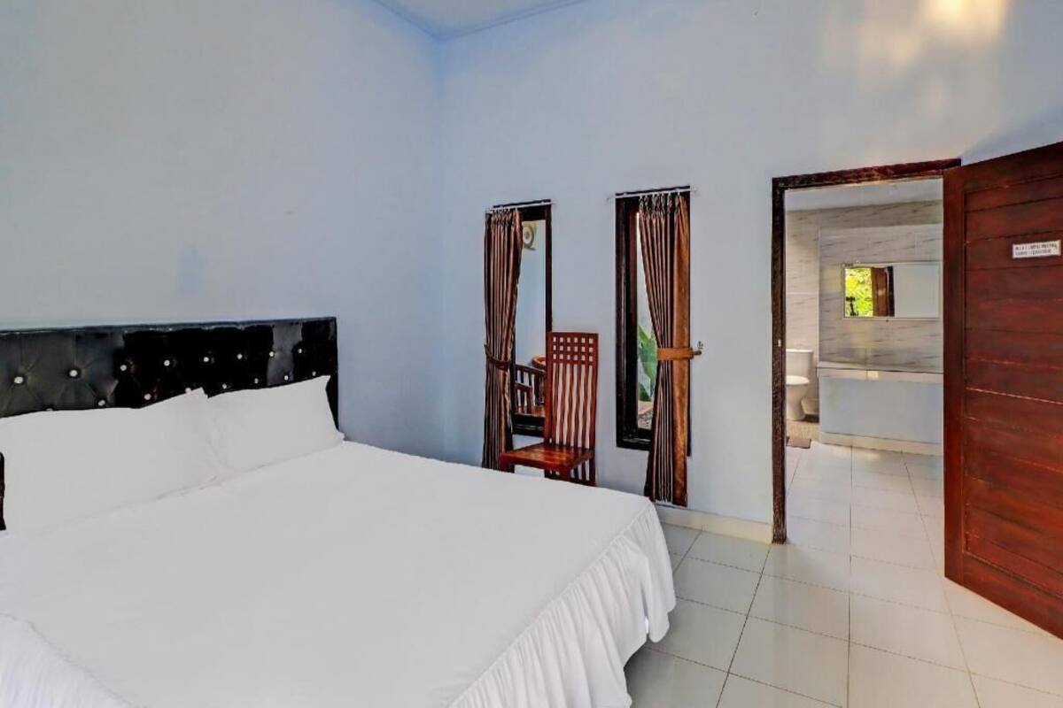 A hotel room with a large bed, a wooden chair, and a bathroom visible through an open door.