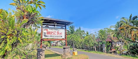 A hotel sign with a roof and a stone base, surrounded by lush greenery and a clear sky.