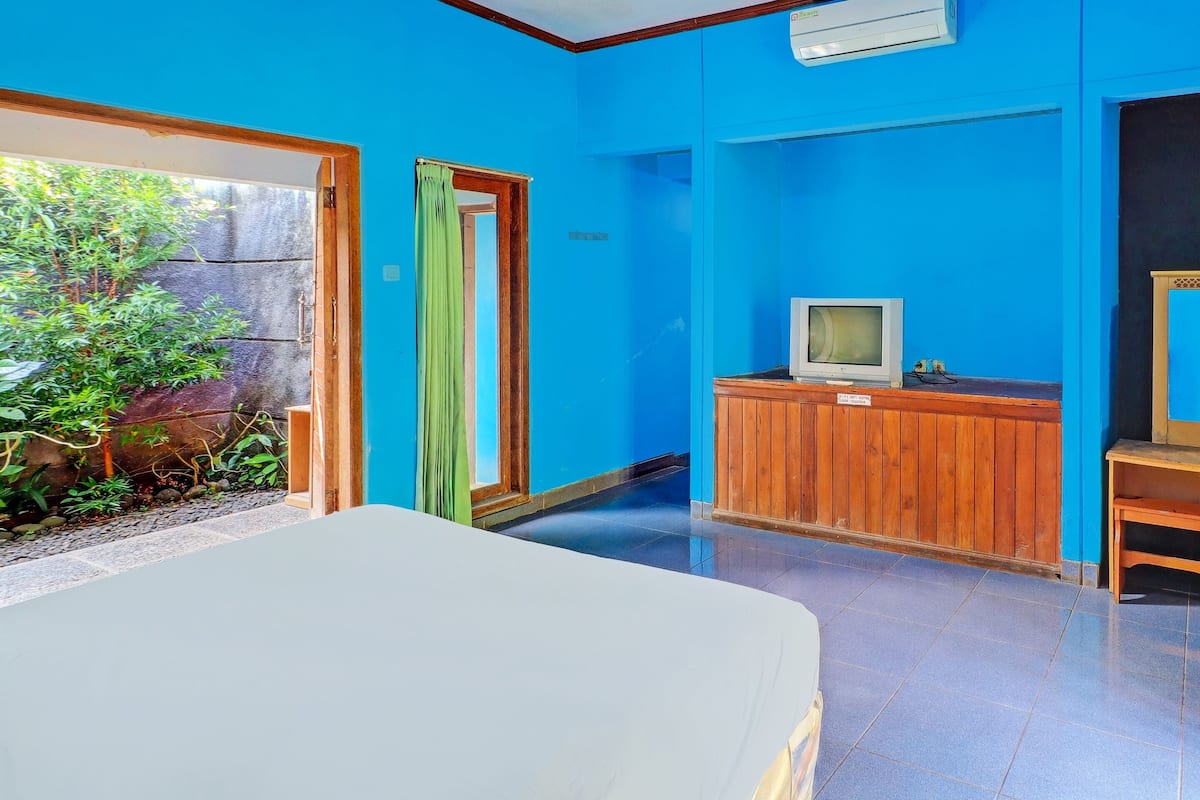 A room with a bed, a television on a wooden cabinet, and a view of a garden through a door.