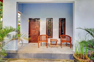 Un espacio de estar al aire libre con techo, con dos sillas de madera y una mesa pequeña, flanqueado por dos puertas con paneles de vidrio decorativo.