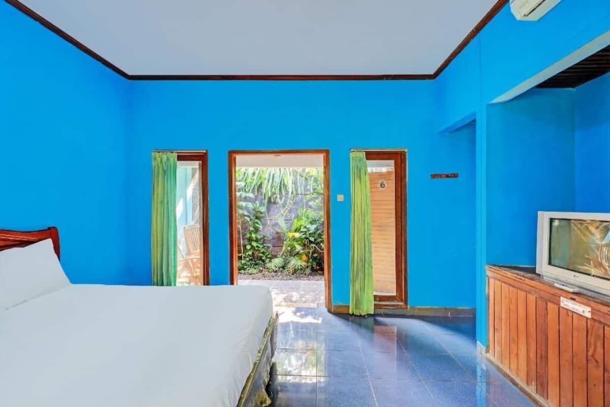 A room with a bed, a television, and a view of a garden through a door.