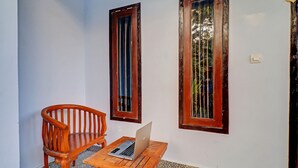 A wooden table with a laptop, a wooden chair, and two windows with wooden frames. - Hotel O Mustika (Negara)