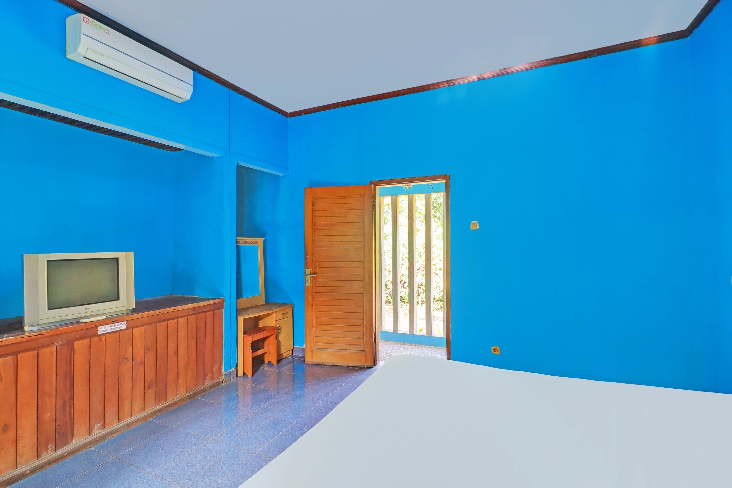 Una habitación con paredes azules, un escritorio de madera, un televisor y una puerta que da al exterior.
