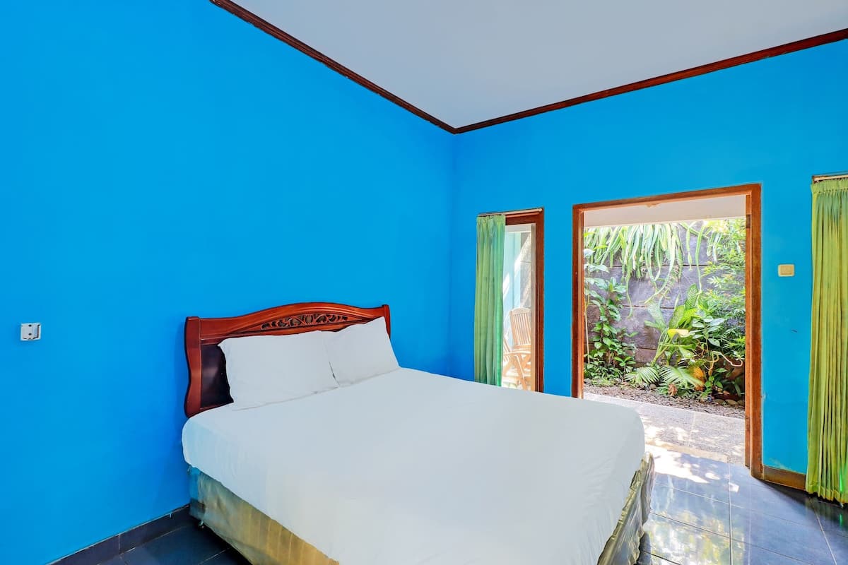 A room with a bed, blue walls, and a view of greenery outside.