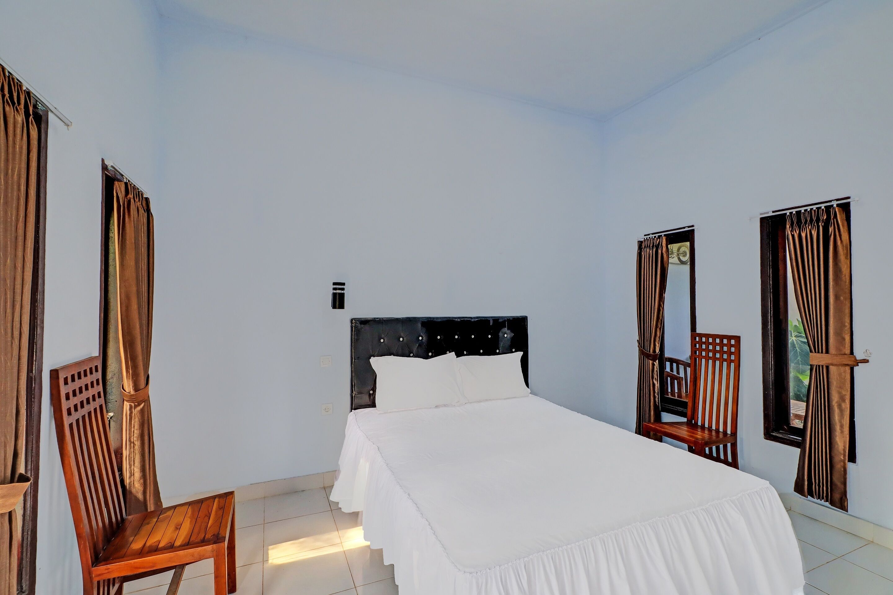 A bedroom with a bed, a wooden chair, and a window with curtains.