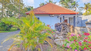 A house with a red tiled roof, surrounded by lush greenery and flowering plants. - Hotel O Mustika (Negara)