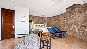 A room with a stone wall, a bed, a glass table, and two blue lounge chairs. - Suite 4 - Casa Samo Conchas Chinas (Puerto Vallarta)