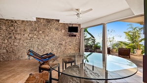 A modern outdoor lounge area with stone walls, a glass table, and lounge chairs. - Suite 4 - Casa Samo Conchas Chinas (Puerto Vallarta)