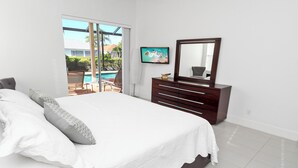 A bedroom with a large bed, a dresser, a TV, and a view of a swimming pool. - Altaira - Top Location, Lake View, Pool, Spa,4 Bed (Naples)