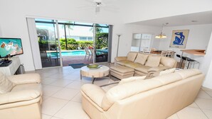 A spacious living room with a beige leather sofa, a coffee table, and a television. - Altaira - Top Location, Lake View, Pool, Spa,4 Bed (Naples)
