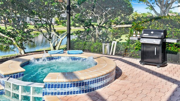 A hot tub with a tiled edge, surrounded by a brick patio, near a grill and a view of a lake. - Altaira - Top Location, Lake View, Pool, Spa,4 Bed (Naples)