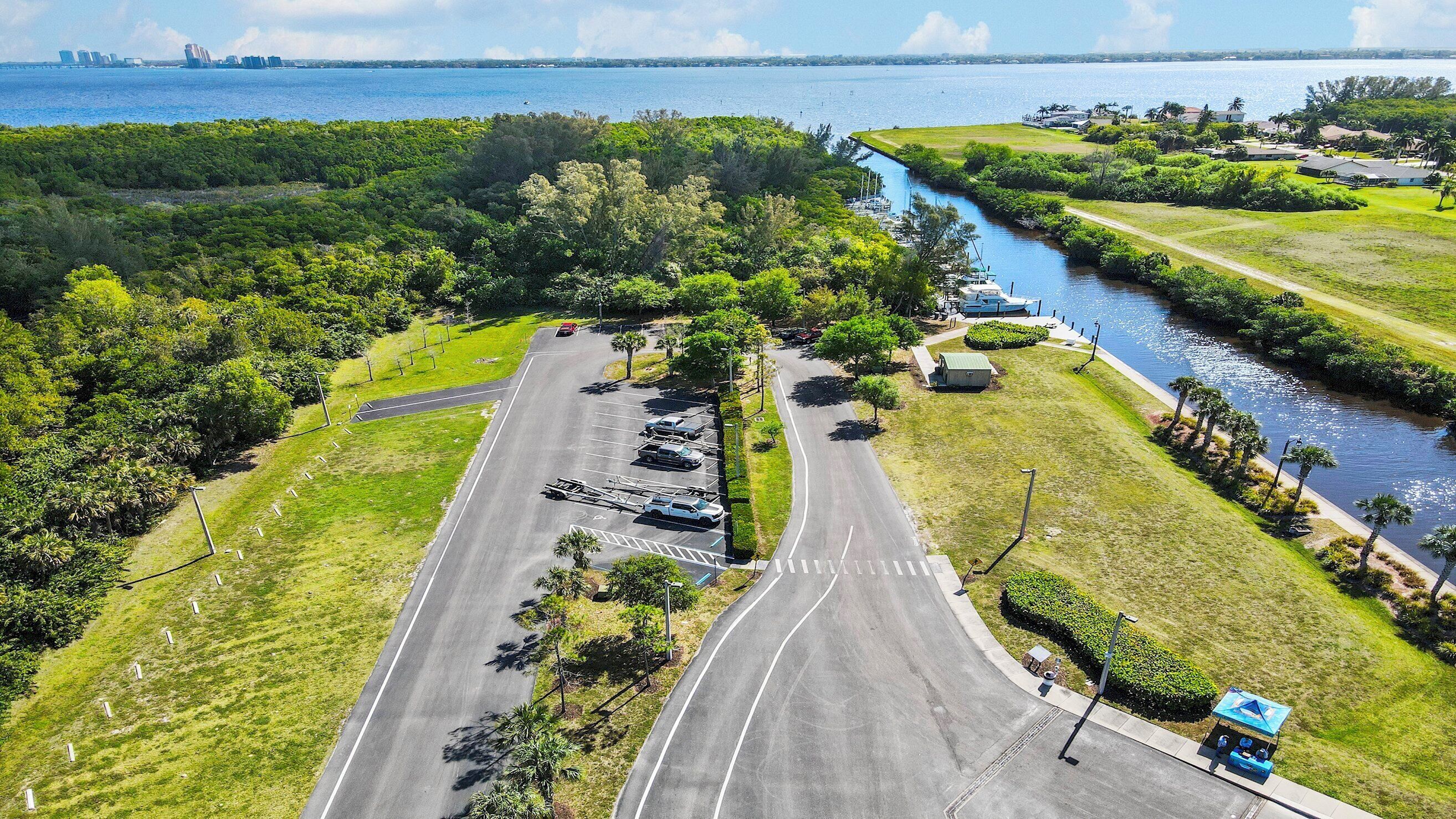 An aerial view of a coastal road with a river running alongside, surrounded by lush greenery and a marina.
