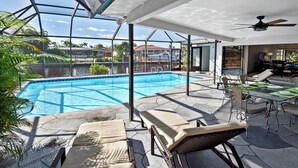 En swimmingpool med liggestole og et spiseområde, omgivet af en glasindhegning.
