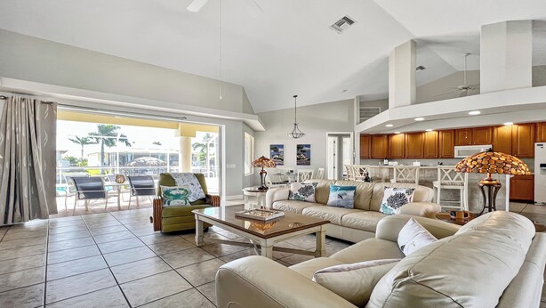 A spacious living room with a large sofa, a coffee table, and a dining area with chairs. There is a kitchen area with wooden cabinets and a ceiling fan. - Boaters Dream, S. Terr, Pool, Yacht Club, Boating (Cape Coral)