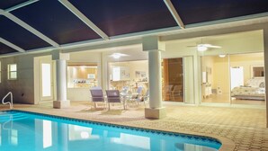An indoor swimming pool area with a patio, a dining area, and a kitchen visible through glass doors. - Boaters Dream, S. Terr, Pool, Yacht Club, Boating (Cape Coral)