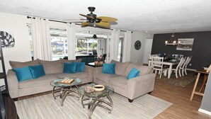 A living room with two sofas, a glass coffee table, a ceiling fan, and a dining area with a table and chairs. - Coral Sunshine - large south terrace with pool/spa (Cape Coral)
