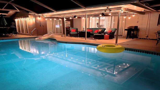 A swimming pool with a yellow float, surrounded by a covered patio area with seating and string lights. - Coral Sunshine - large south terrace with pool/spa (Cape Coral)